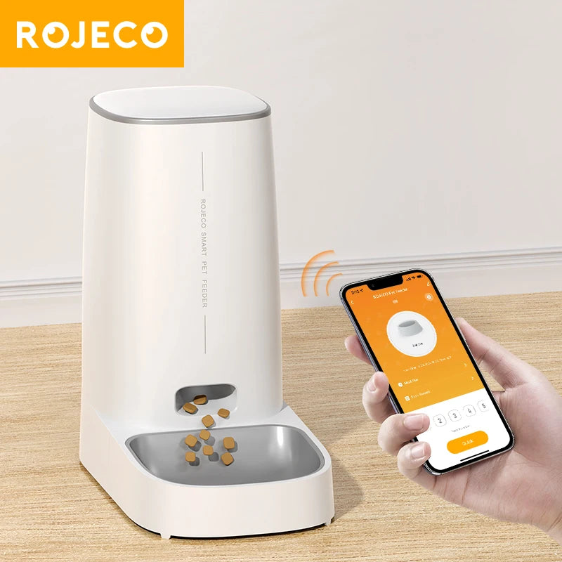 White ROJECO 4L automatic cat feeder dispensing dry kibble while a hand controls it from the app on a smartphone