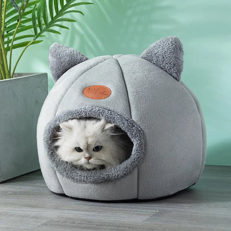 Light grey cat cave bed with a long-haired white cat inside, styled against a green wall