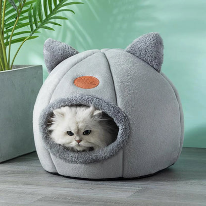 Light grey cat cave bed with a long-haired white cat inside, styled against a green wall